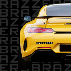 Brazzers car sticker with Brazzers written on a black background. The sticker is pictured on the back of a yellow sports car.